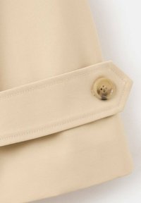 Tessuto beige con una cinghia cucita e un bottone traslucido a quattro fori fissato vicino all'estremità inclinata della cinghia.