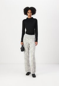 Black ribbed long-sleeve top paired with light gray patterned sweatpants and black footwear. Model holds a small black handbag.