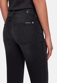Black denim jeans with a fitted design, featuring a mid-rise waist, two back pockets, and subtle stitching details.