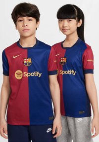Crvene i plave Barcelonine dresove s zlatnim akcentima; Nike logo na prsima i Spotify brendiranje. Kratki rukavi s dizajnom okruglog izreza.