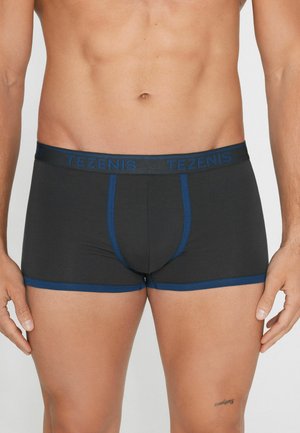 Męski tors noszący czarne bokserki z niebieskim wykończeniem i paskiem w talii, z nazwą marki „TEZENIS” w niebieskich literach.