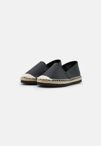 Černé espadrilky na slip-on s béžovými tkanými špičkami a podrážkami s jutu na bílém pozadí, viděné z přední pravé úhlu.