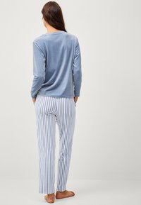 Blauwe velours lange mouwen top met een ronde hals, gecombineerd met witte en lichtblauwe gestreepte pyjamabroek met een relaxte pasvorm en zakken.