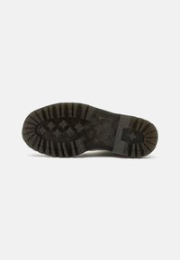 Suela de goma negra con surcos profundos, con un patrón de estrellas y superficie texturizada. Incluye una entresuela marrón claro y detalles de marca.
