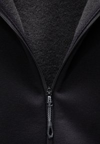 Giacca nera con chiusura a zip. Fodera in morbido fleece grigio visibile all'interno del colletto. Tessuto testurizzato con superficie esterna liscia. Dettaglio della zip resistente.