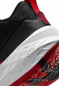 Baskets noires avec une tige synthétique texturée, semelle en caoutchouc blanche, accents rouges et un motif de semelle sur la partie inférieure.