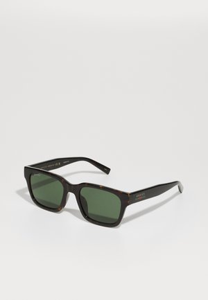 Óculos de sol tartaruga com lentes verdes, armação quadrada e detalhes em dourado com o logótipo da Gucci na haste. Acabamento brilhante.
