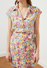 Kwiatowa sukienka z krótkim rękawem w pastelowych kolorach. Posiada zapięcie na guziki z przodu, pasek w talii oraz luźny krój. Wykonana z lekkiego materiału.