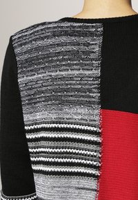 Maglione lavorato a maglia con un design a collage composto da sezioni di colori nero, rosso e grigio testurizzato, che mette in mostra texture e punti vari.
