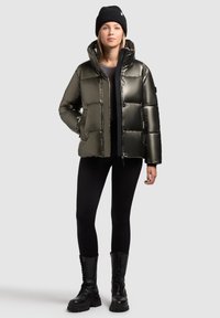 Skinnende olivengrøn puffjakke med firkantet design, lynlås, hætte og sidelommer, parret med sorte leggings og kampstøvler.