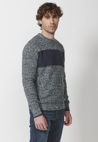 Suéter de punto en navy y gris con un diseño texturizado, que presenta una banda sólida en navy en el pecho, puños y dobladillo acanalados.