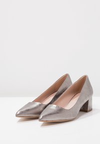 Pompes argentées métalliques à talons blocs avec un bout pointu, présentant une surface lisse et brillante et un dos légèrement texturé pour une meilleure accroche.