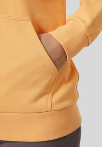 Bluza z kapturem w kolorze miodowym z kieszenią typu kangur. Miękki materiał, ściągacze przy mankietach i pasie. Szwy widoczne wokół kieszeni.