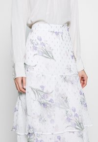 Durchsichtiger weißer Rock mit pastellfarbenen Blumenmustern, silbernen Akzenten, geschichtetem Design und strukturierter Oberfläche mit kleinen Pailletten.