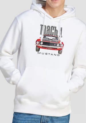 Person wearing a white hoodie with a red 1969 Mustang car graphic and "Mach 1 Mustang" text, hands in front pocket, paired with blue jeans.
