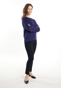 Granatowy sweter, fakturowany materiał, okrągły dekolt; w połączeniu z czarnymi dopasowanymi spodniami i błyszczącymi czarnymi baletkami. Modelka stoi pewnie z ramionami skrzyżowanymi.