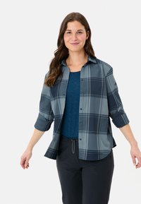 Camicia a quadri blu e grigia con maniche arrotolate, apertura con bottoni, abbinata a una parte superiore blu unita e pantaloni scuri, esposta su uno sfondo bianco.