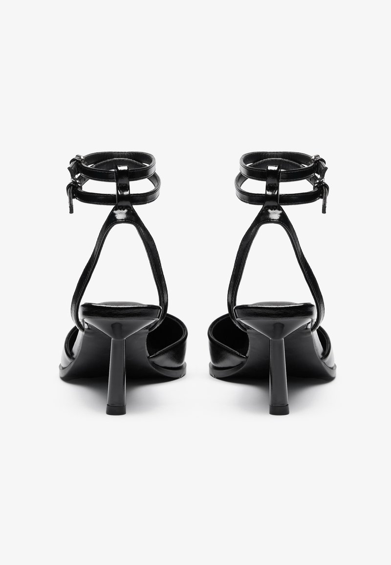 Zwarte gepatineerde leren hoge hak sandalen met enkelbandjes, open teen en een slanke, spitse vorm. Gestructureerde bandjes en een smalle hak.