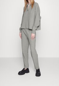 Suéter de canalé gris claro, con cuello de media cremallera, combinado con joggers ajustados a juego. Unos zapatos mocasines negros y gruesos completan el conjunto.