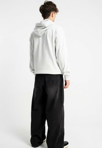 Biała bluza z kapturem i długimi rękawami, noszona z luźnymi czarnymi dżinsami. Gładka tekstura, minimalistyczny design, brak widocznych wzorów.