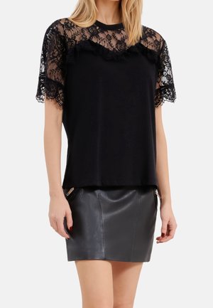 Femme portant un haut noir en dentelle à manches courtes avec des motifs floraux, assorti à une mini-jupe en cuir noir avec des détails de zip.