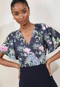 Blommig blus med djup V-neck och korta, vida ärmar. Det marinblå tyget har livliga rosa, lila och gröna blommönster.