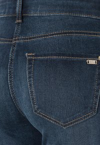 Tummansiniset farkut, joissa on kontrastivärinen oranssi tikkaus, takataskussa merkki ja sileä rakenne.