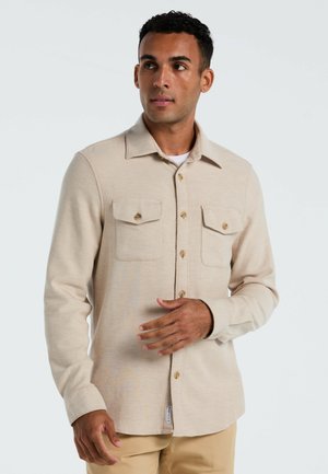Beige langza sleeve shirt met twee borstzakken, knoopsluiting, kraag en een gestructureerde stof. Kenmerkend zijn de accenten van gouden knopen.