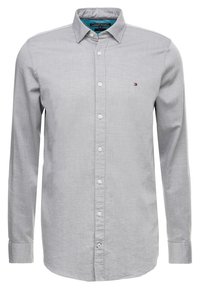 Camisa de manga larga color gris claro con botones, confeccionada en tela texturizada. Cuenta con cuello con solapa, cierre de botones y un pequeño logotipo en el pecho.