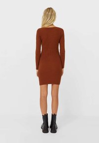 Robe longue à manches longues en tricot côtelé marron, silhouette ajustée, longueur genou, texture lisse, associée à des bottines noires.
