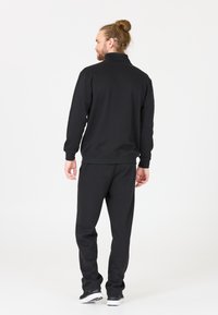 Zwarte trainingsoutfit met een top met ritssluiting en een elastische tailleband. De stof lijkt zacht met een gladde textuur. Contrasterende schoenen.