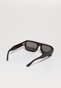 Ochelari de soare cu model țestoasă, cu lentile dreptunghiulare, nuanța gri și accente aurii pe brațe. Finisaj texturat, cadru din plastic rezistent.
