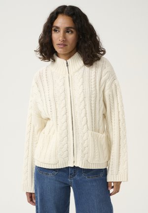 Cardigan bianco lavorato a maglia con zip e colletto alto, caratterizzato da motivi a trecce e due tasche frontali. Tessuto testurizzato con maniche ampie.