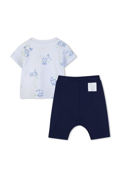 Chemise blanche pour bébé à manches courtes avec des tigres en dessin animé bleus et un short bleu marine avec un petit patch tigre assorti sur le devant.