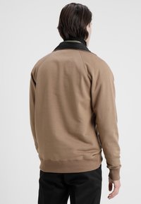 Brązowa bluza z czarnym kołnierzem, o luźnym kroju, długich rękawach i ściągaczach przy mankietach i u dołu. Gładka tekstura, prosty design.