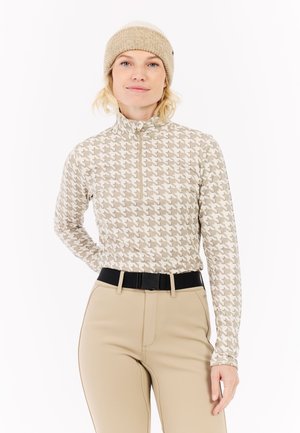 Beige Langarmoberteil im Hahnentrittmuster mit einem halben Reißverschluss, kombiniert mit beigen Hosen und einer hellbraunen Strickmütze. Schwarzer Gürtel als Akzent.