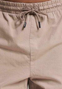 Beige lehké šortky s elastickým pasem a šňůrkou na stažení. Texturovaná látka má jemný mřížkový vzor. Nejlépe bez viditelných kapes.