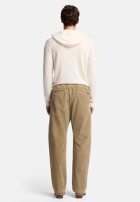 Beige Corduroypants im entspannten Schnitt, mit zwei Backtaschen, kombiniert mit einem weißen Hoodie mit einer weichen, gefütterten Kapuze.