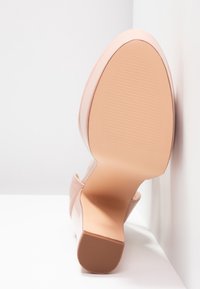Petite chaussure à talon beige vue par la semelle, montrant un dessous texturé et un talon carré sur fond blanc.