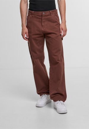 Brown cotton cargo pants with a relaxed fit, featuring front pockets, button closure, and slight texture. Paired with white sneakers.