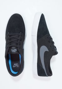 Musta samettinen urheilukengät matalalla varrella, valkoiset kumipohjat ja harmaa Nike-swoosh -koriste. Varustettu mustilla nauhoilla ja sinisellä sisäpuolella.
