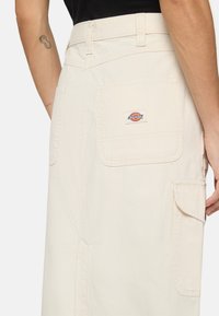 Ljusbeige kjol med rak skärning, som har framfickor och ett litet Dickies-logopatch på bakfickan. Bomullstyg, avslappnad design.