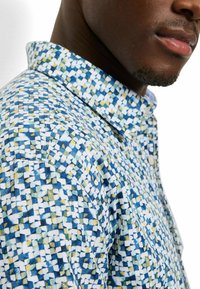 Kurzarmhemd mit einem geometrischen Muster in Blau, Weiß und Gelb. Der Stoff wirkt leicht, mit einem klassischen Kragen und sauberer Naht.