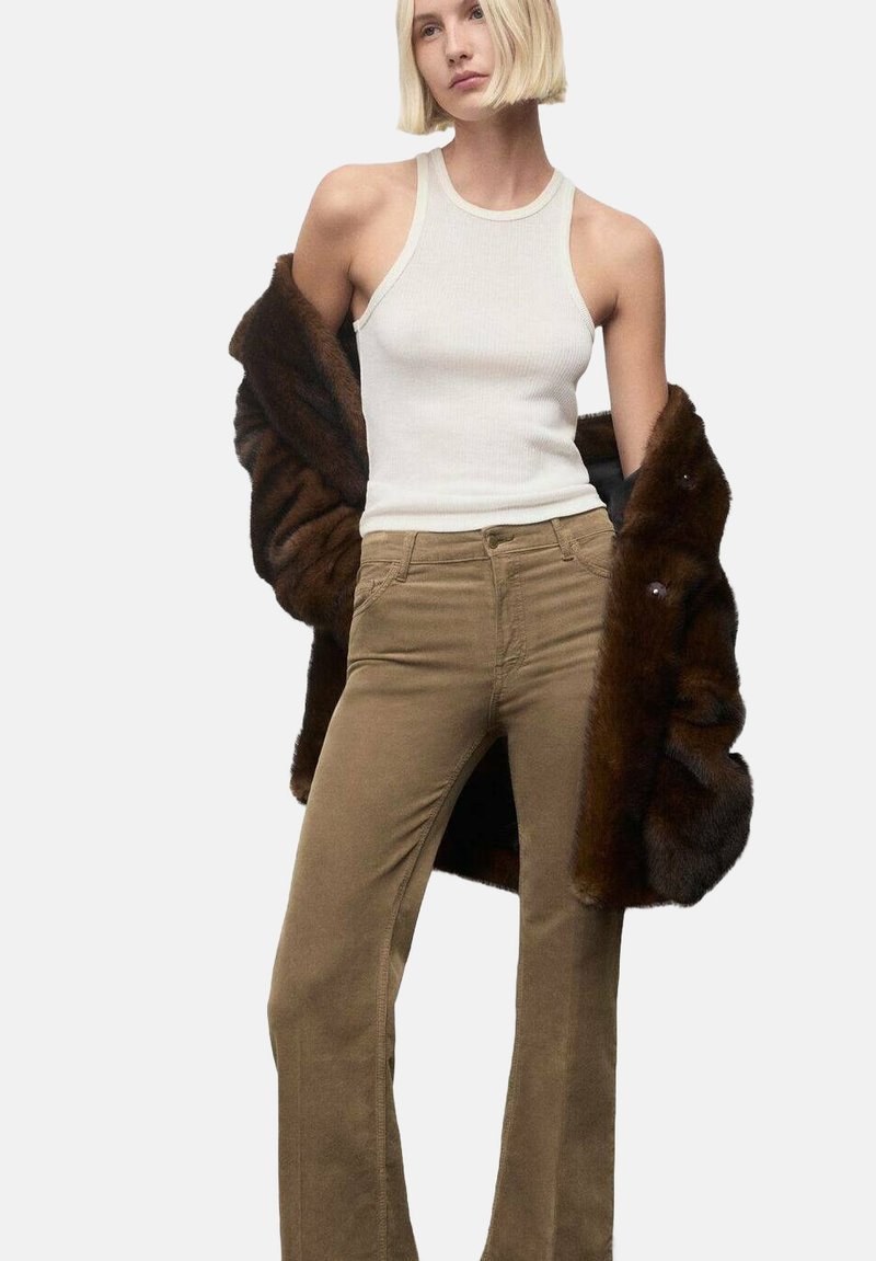 Top sin mangas de canalé blanco, abrigo de piel sintética marrón y pantalones acampanados beige. El conjunto presenta una forma ajustada y texturas suaves sin patrones visibles.