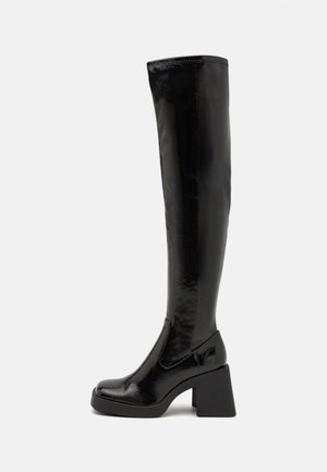 Bottes noires en cuir verni montant jusqu'au genou, avec un talon bloc épais, un bout arrondi et un design sans coutures. Texture lisse avec un léger brillant.
