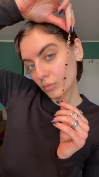 Σκουλαρίκι αλυσίδα χρυσού με μαύρες και διάφανα χάντρες, με κούμπωμα. Φοριέται από άτομο με μπλε βαμμένα νύχια και ασημένια δαχτυλίδια.