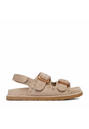 Beige Wildledersandale mit zwei verstellbaren Schnallen, Knöchelriemen und dekorativen Nieten auf einer flachen Gummisohle.