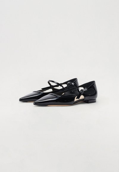 Ballerines noires en cuir verni avec bouts pointus, dotées d'une bride de cheville et d'un petit nœud décoratif sur le côté extérieur, texture lisse, design minimaliste.