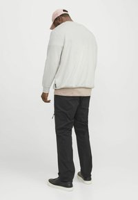 Lichtgrijze sweatshirt met een relaxte pasvorm, bovenop een beige top; gecombineerd met zwarte cargobroeken met zijritszakken en zwarte sneakers.