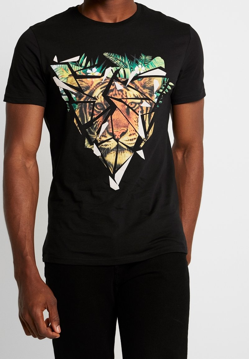 T-shirt en coton noir avec un design graphique d'un visage de lion entouré de formes géométriques et d'accents de feuillage vert.